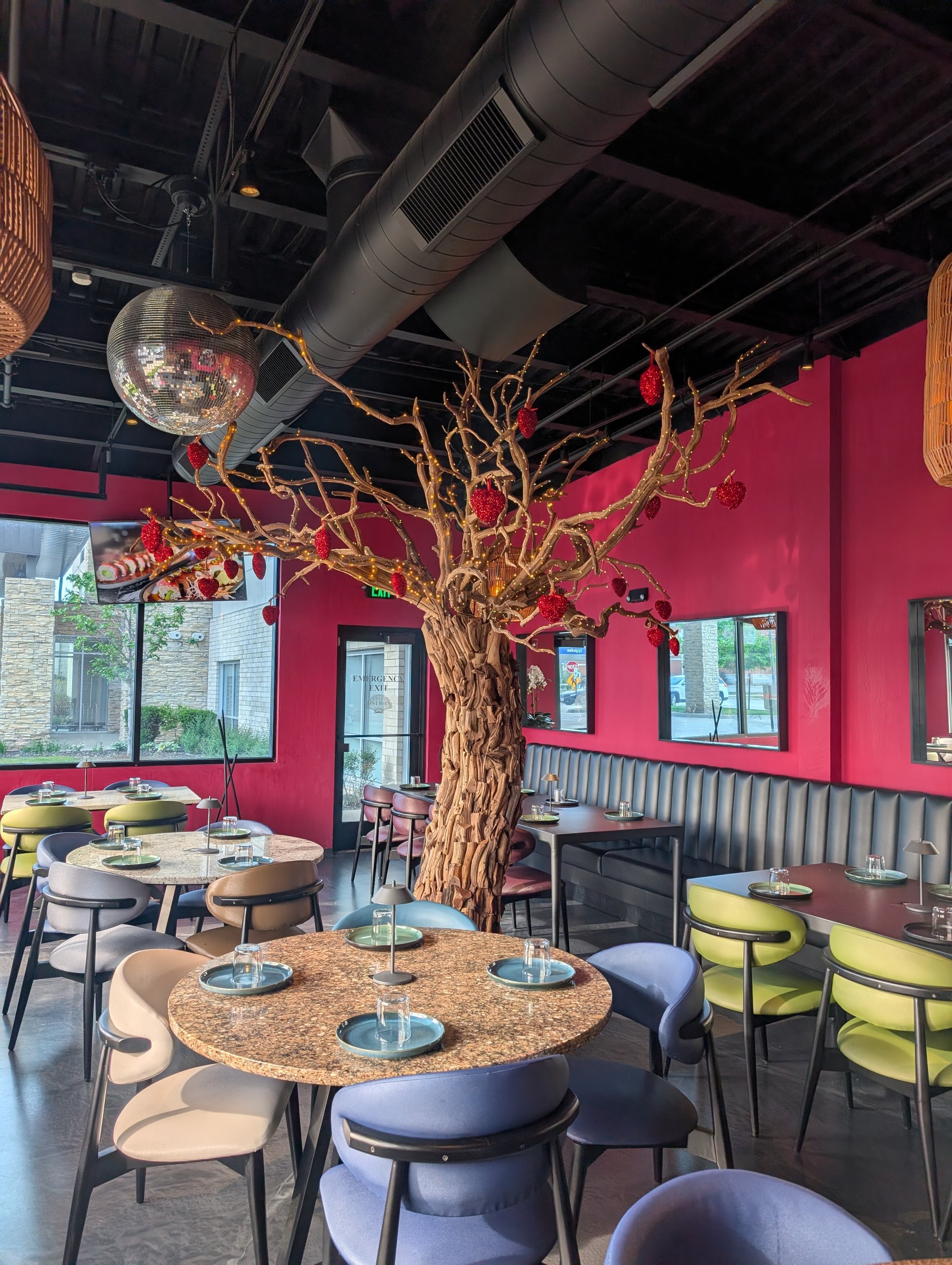 Pink-walled patio dining room at Ostras Lounge with a centerpiece tree wrapped in red lanterns