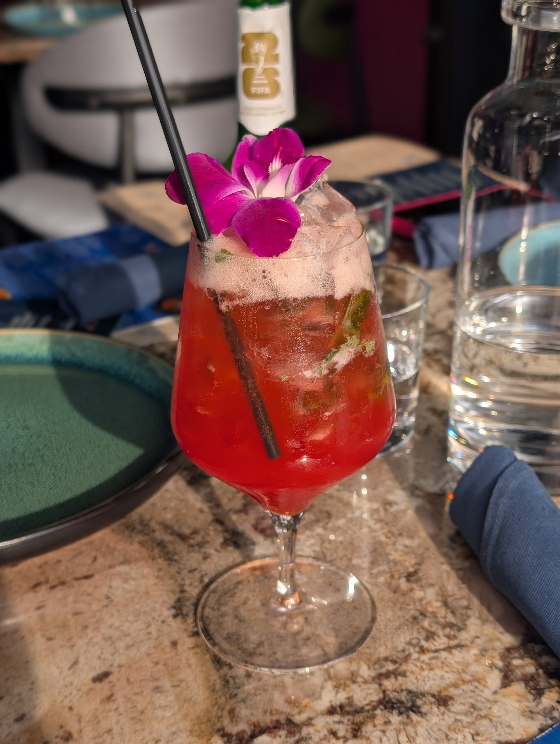 Bright red mocktail in a stemmed glass topped with an edible purple orchid at Ostras Lounge