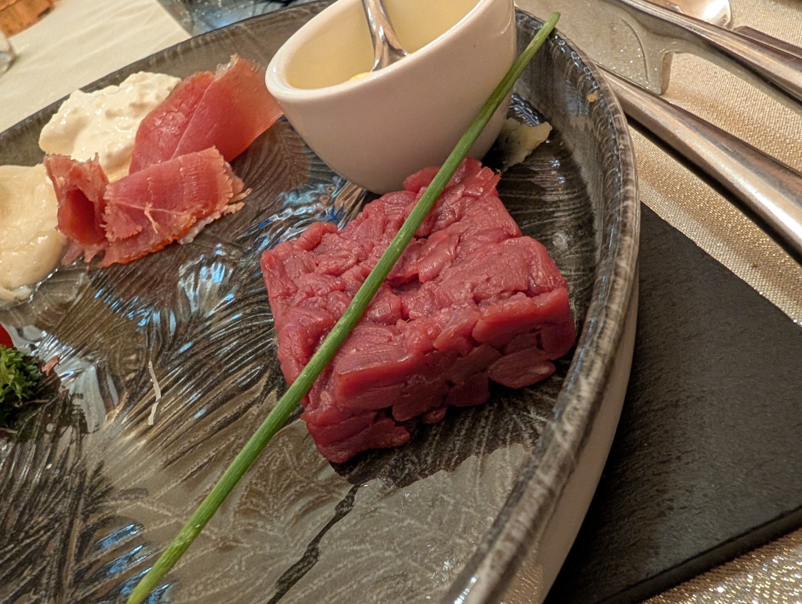 Beef tartare cubes with chive garnish, plated alongside thin-sliced carpaccio and cream sauce at Ristorante Ad Hoc, Rome