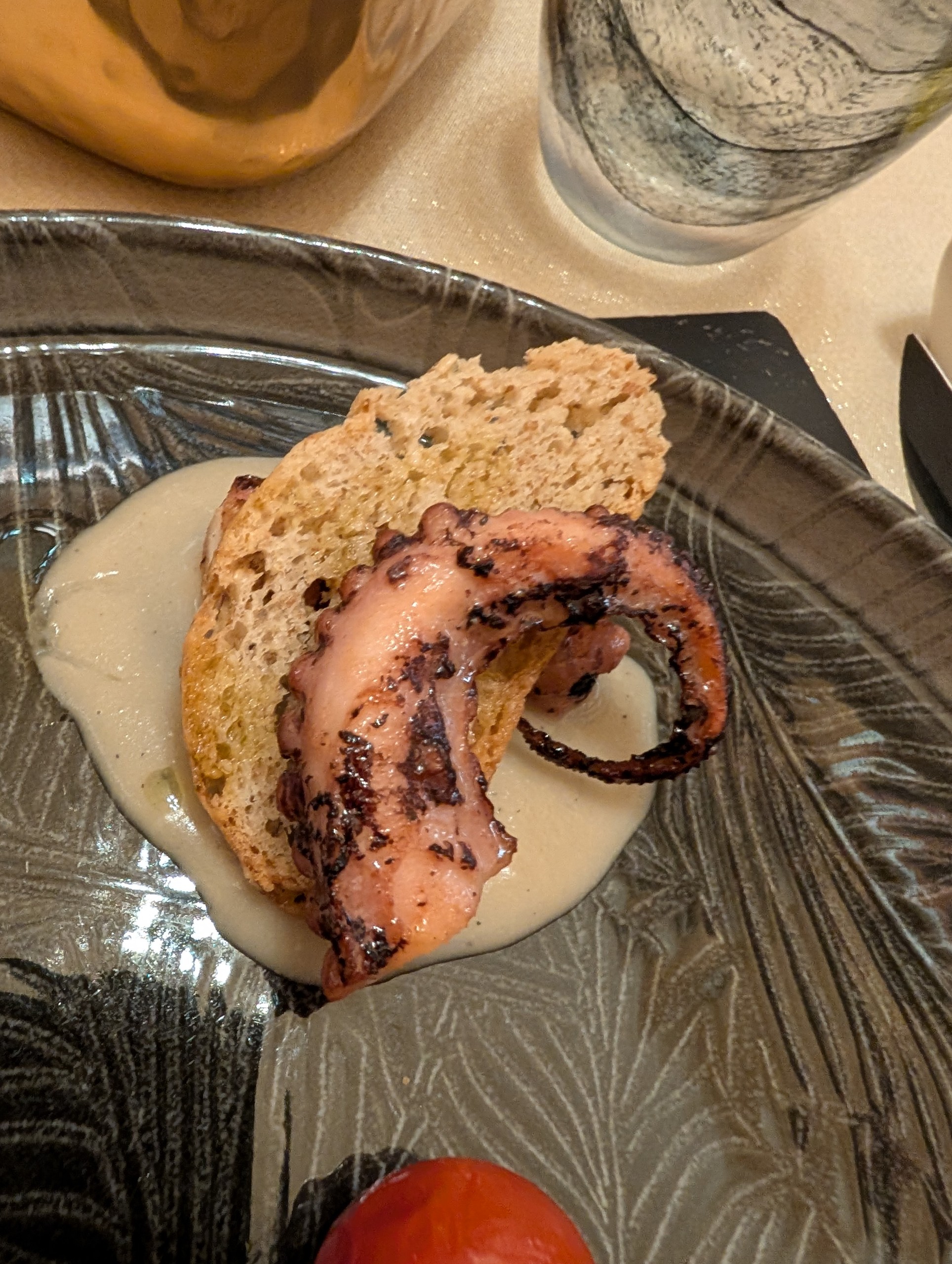 Grilled octopus tentacle on toasted bread, served on a creamy sauce on a dark textured ceramic plate at Ristorante Ad Hoc, Rome