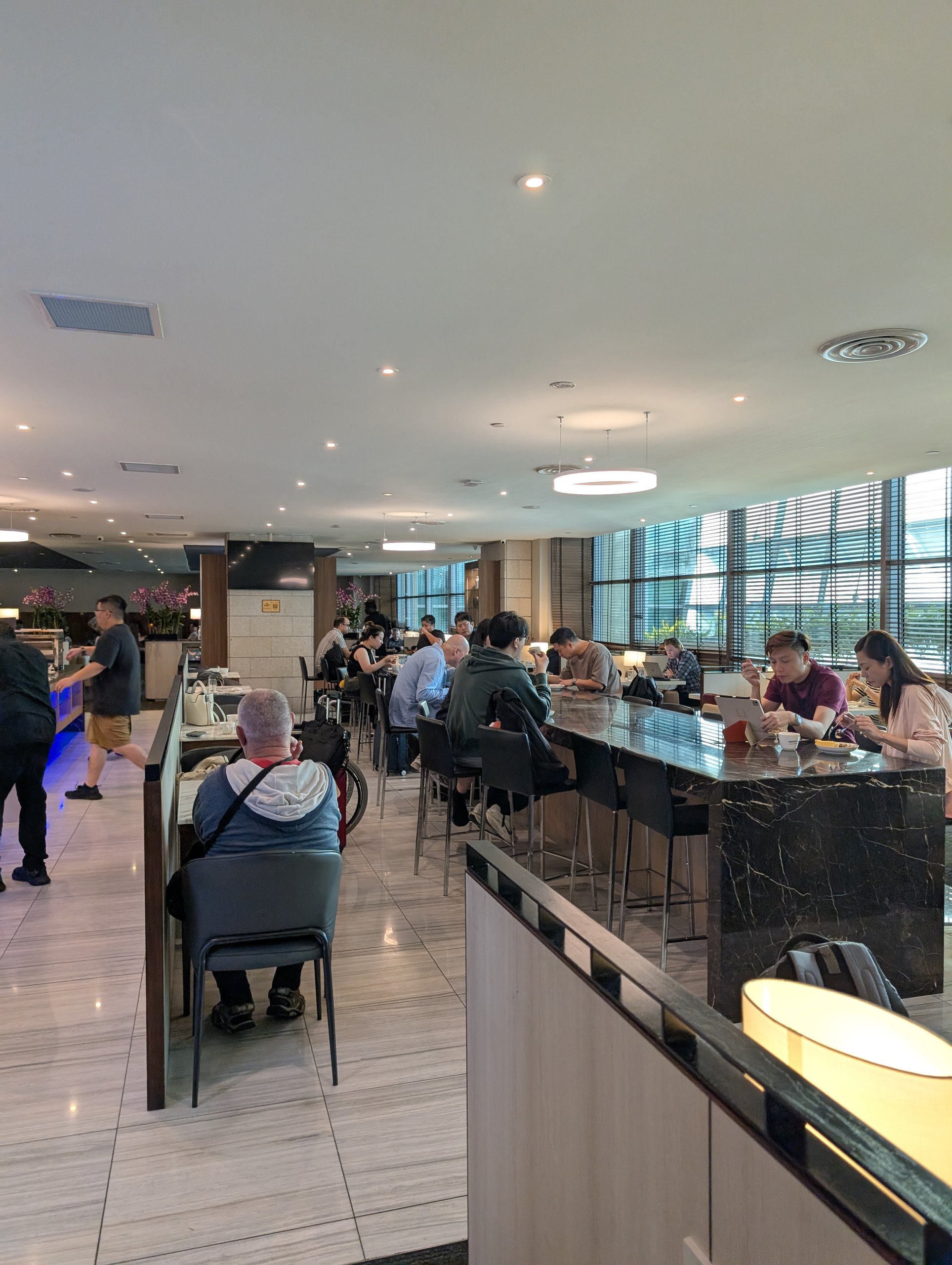 Long view down the bar counter with travelers eating and working at the SATS Premier Lounge Changi T2