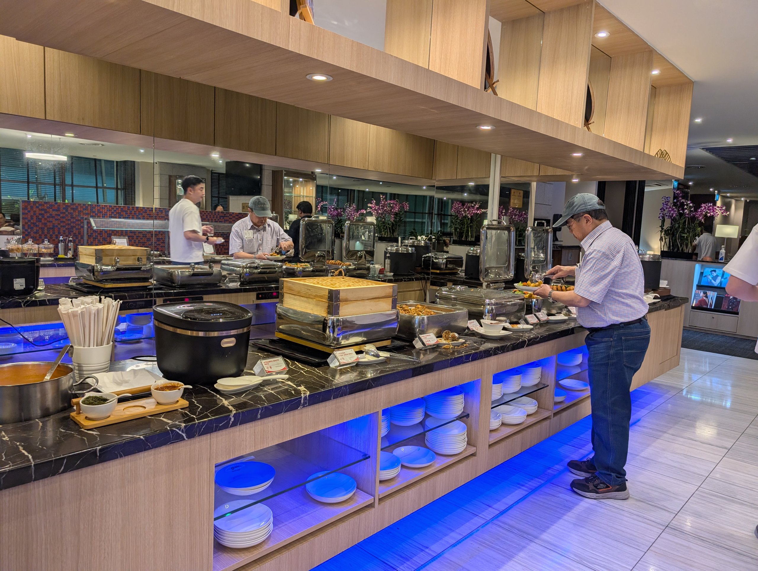 Hot buffet counter at the SATS Premier Lounge Changi T2 with chafing dishes, dumpling baskets, and live attendants