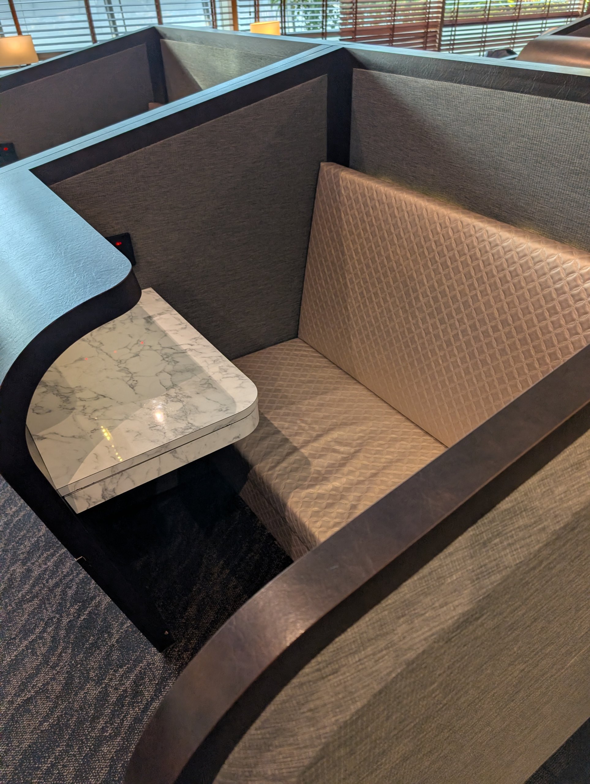 Close up of a single semi private nook booth with a marble side table and quilted backrest at the SATS Premier Lounge Changi T2