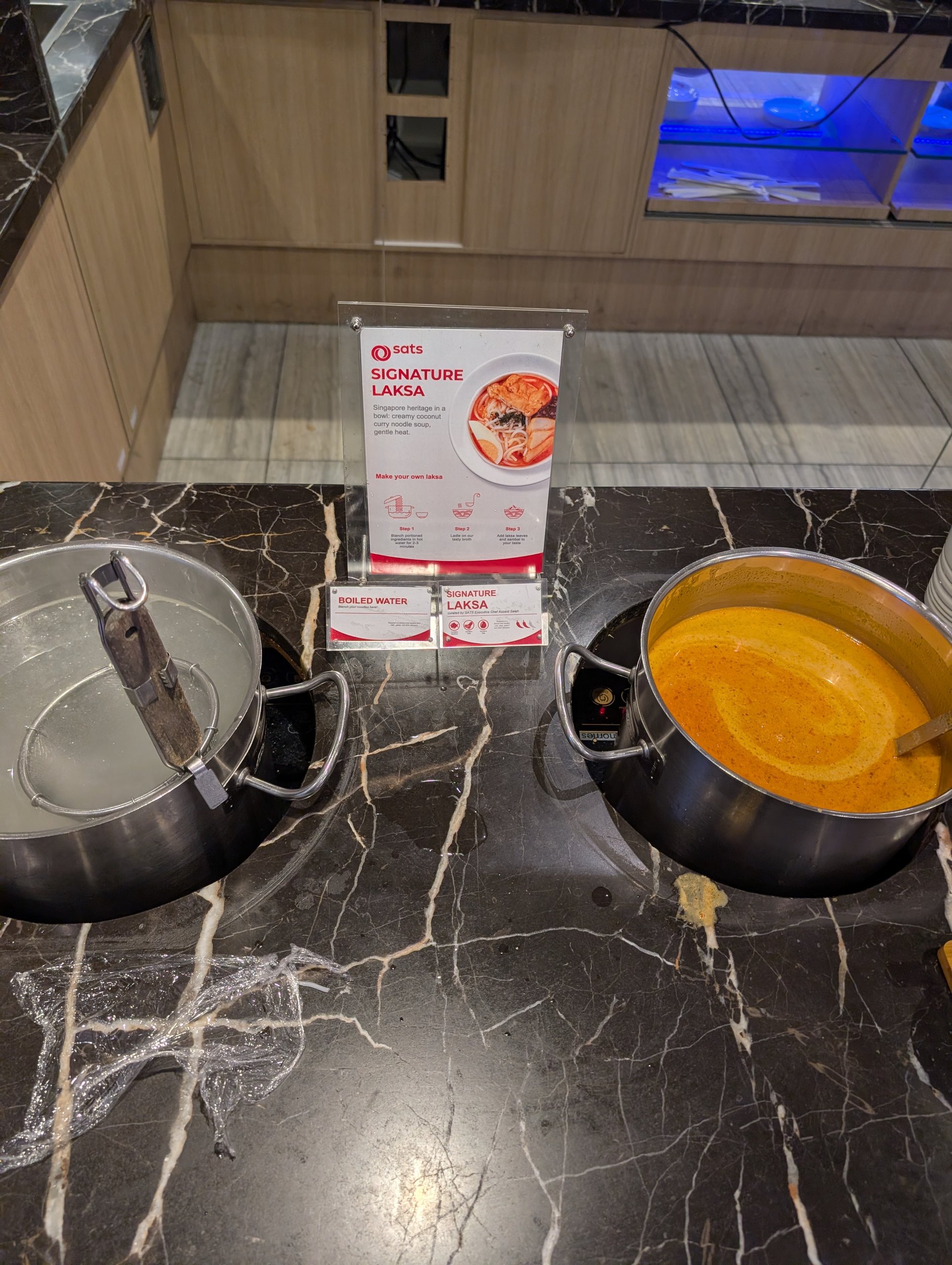 Dedicated signature laksa station with broth pot, boiled water pot, and signage at the SATS Premier Lounge Changi T2