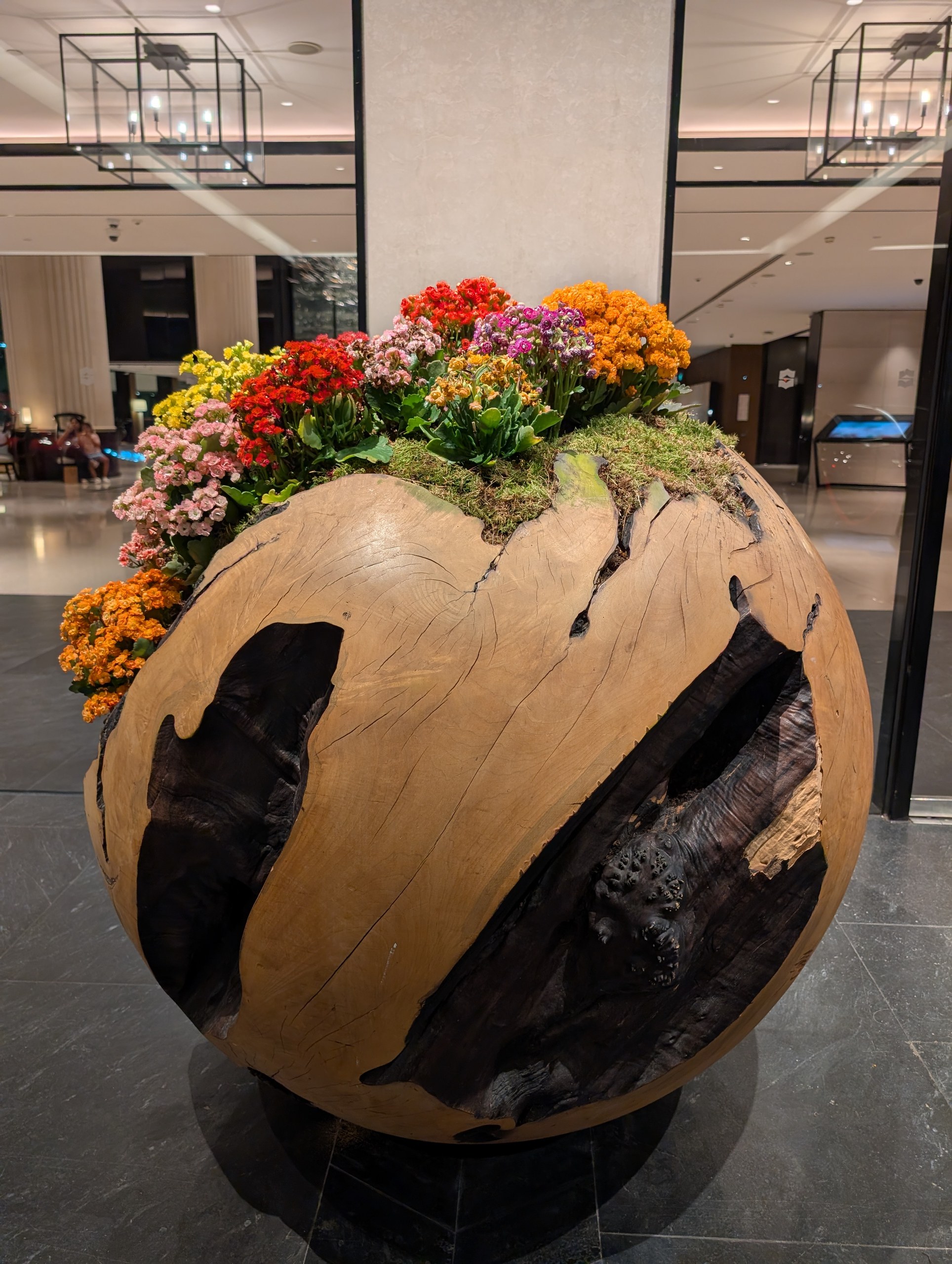 Hand-carved wooden sphere planter with kalanchoes and orchids in the Shangri-La Singapore lobby.