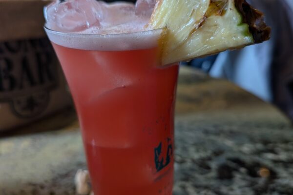 The original Singapore Sling at Long Bar in a branded hurricane glass with a pineapple wedge and cherry garnish