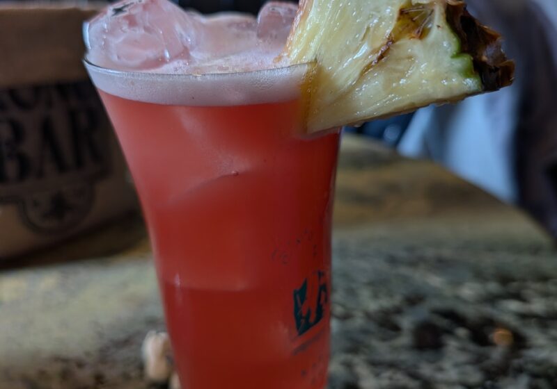 The original Singapore Sling at Long Bar in a branded hurricane glass with a pineapple wedge and cherry garnish