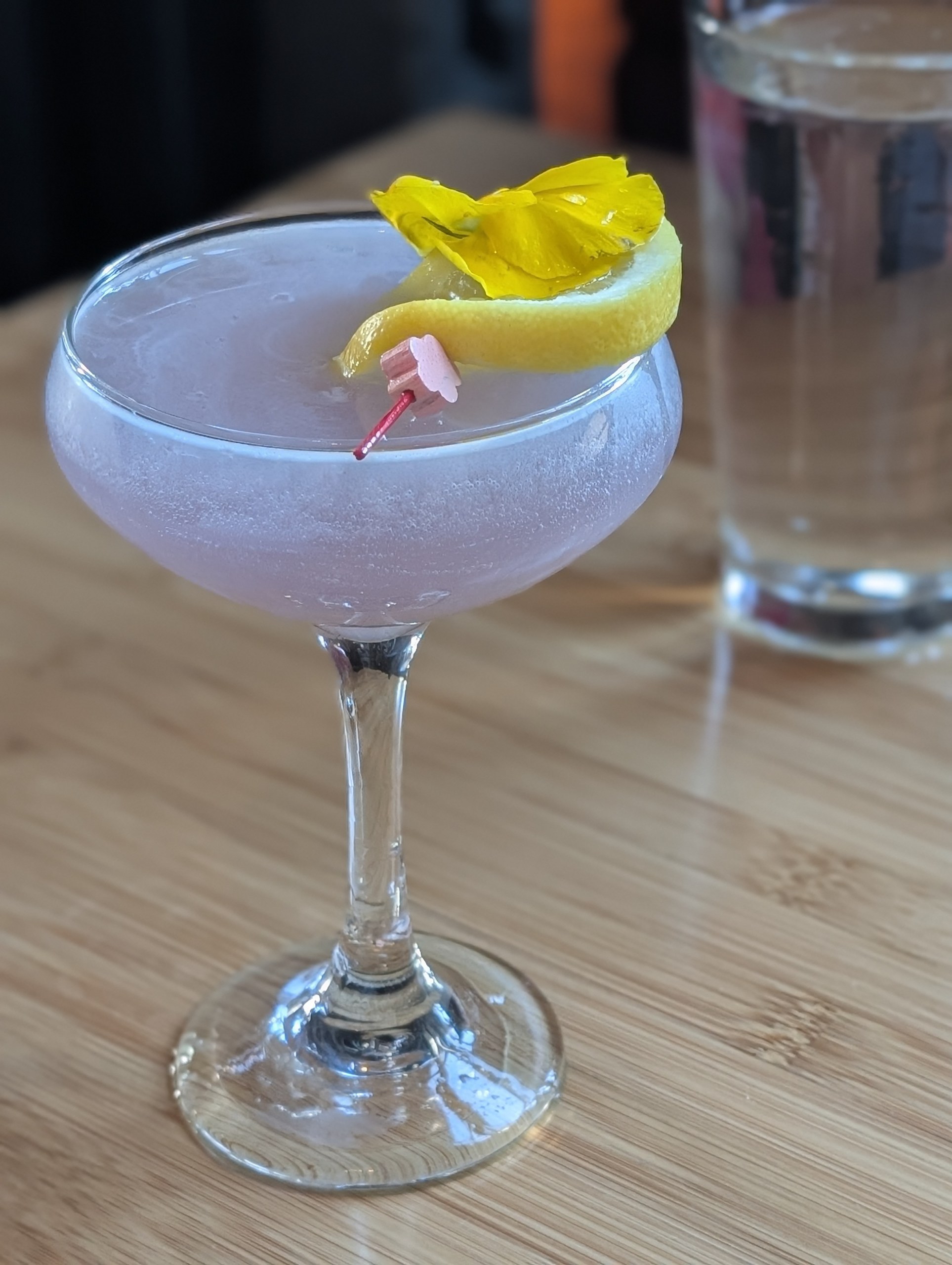 Empress' Kiss cocktail at Sushi Roku Las Vegas in a coupe glass with lavender color, lemon twist, and pretty yellow flower garnish