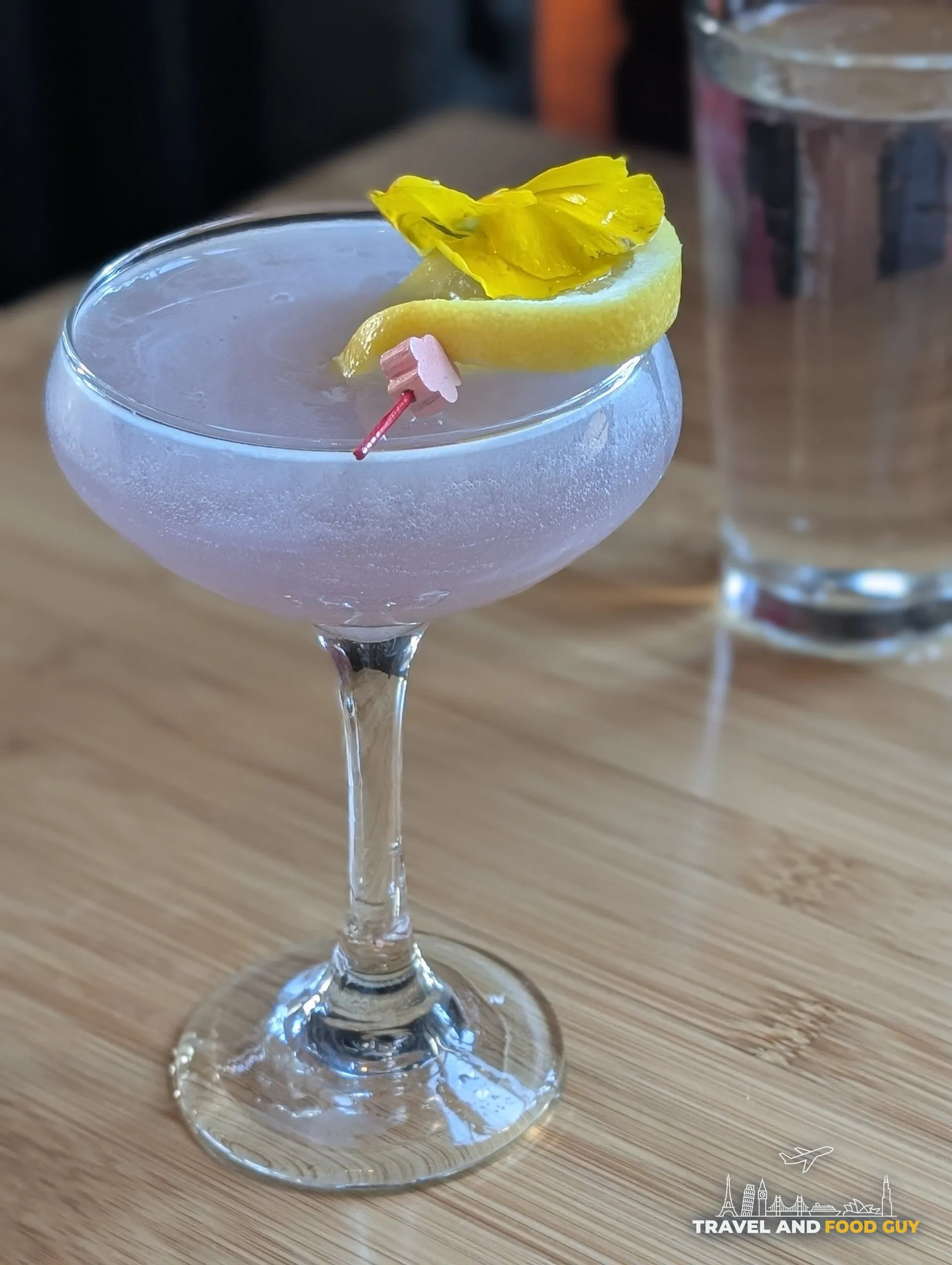 Empress' Kiss cocktail at Sushi Roku Las Vegas in a coupe glass with lavender color, lemon twist, and pretty yellow flower garnish