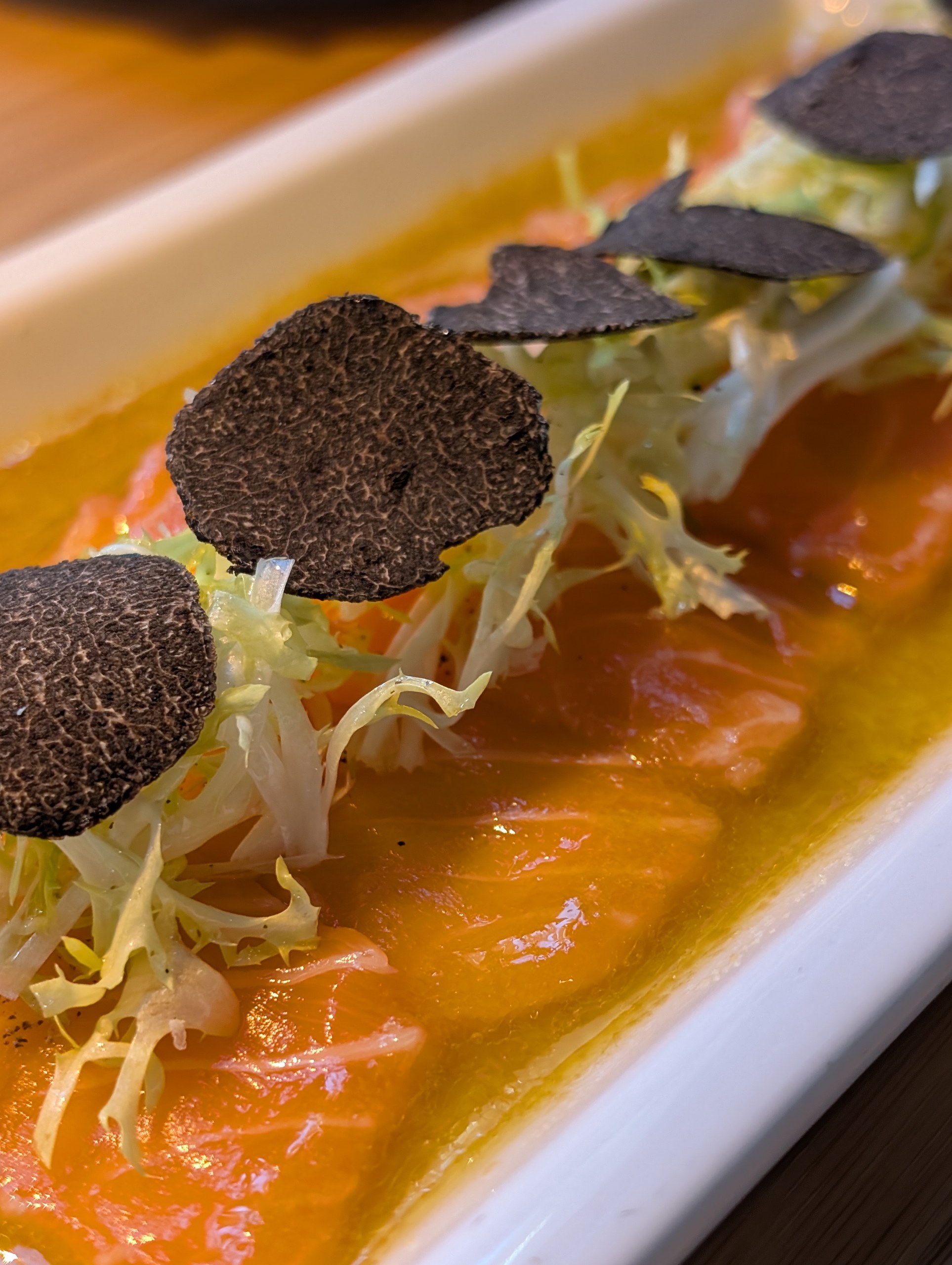 Salmon Truffle Carpaccio at Sushi Roku Las Vegas with thinly sliced salmon, frisée, large black truffle rounds, and citrus oil