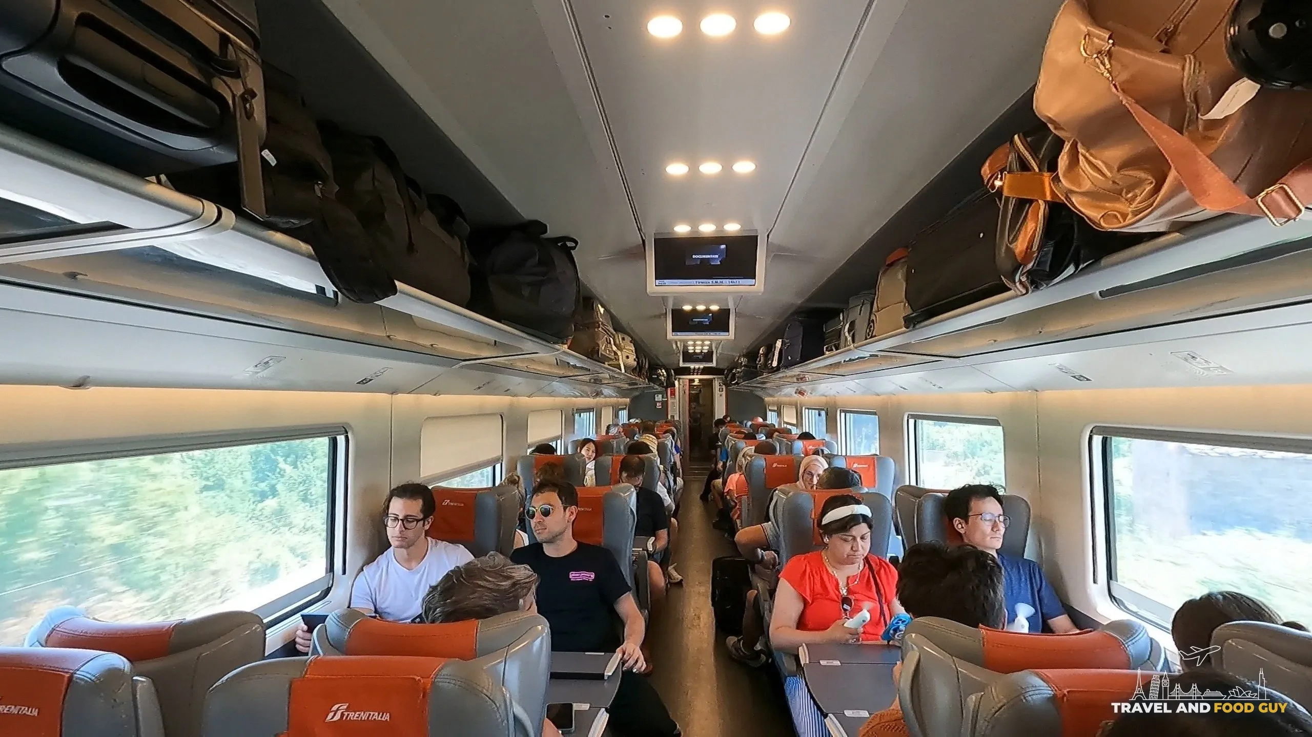Wide interior view of a Trenitalia Frecciarossa high-speed train cabin with passengers