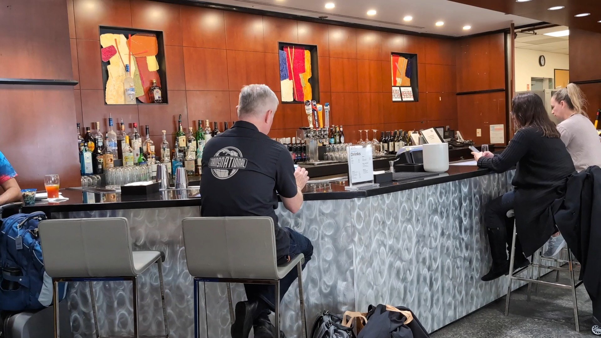 Close-up of the bar at the United Club at IAH Gate C33 with bottles lined up behind the bartender and travelers in bar stools.