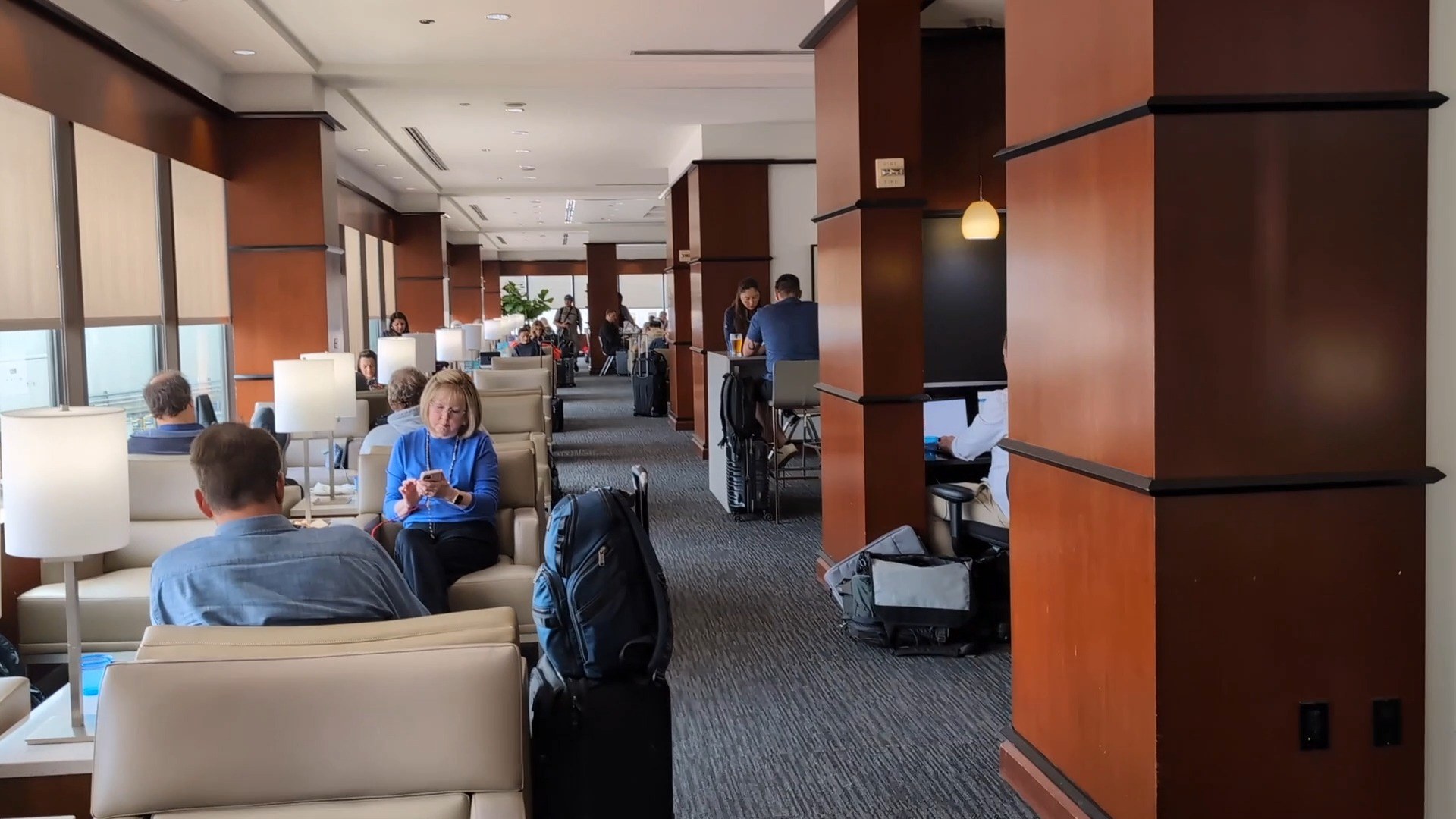 Main seating area at the United Club at IAH Gate C33, with cherry-wood columns and travelers working at lounge chairs and tables.