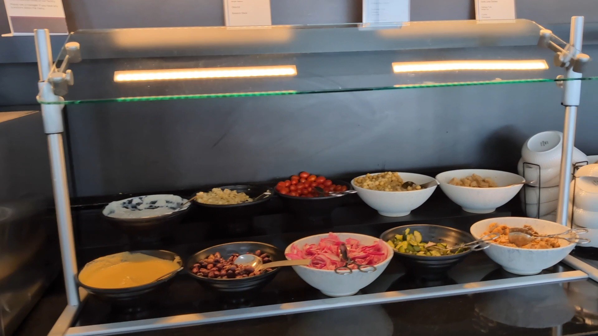 Salad bar at the United Club at IAH Gate C33 with bowls of cherry tomatoes, beans, pickled onions, cucumbers, and grain salads.