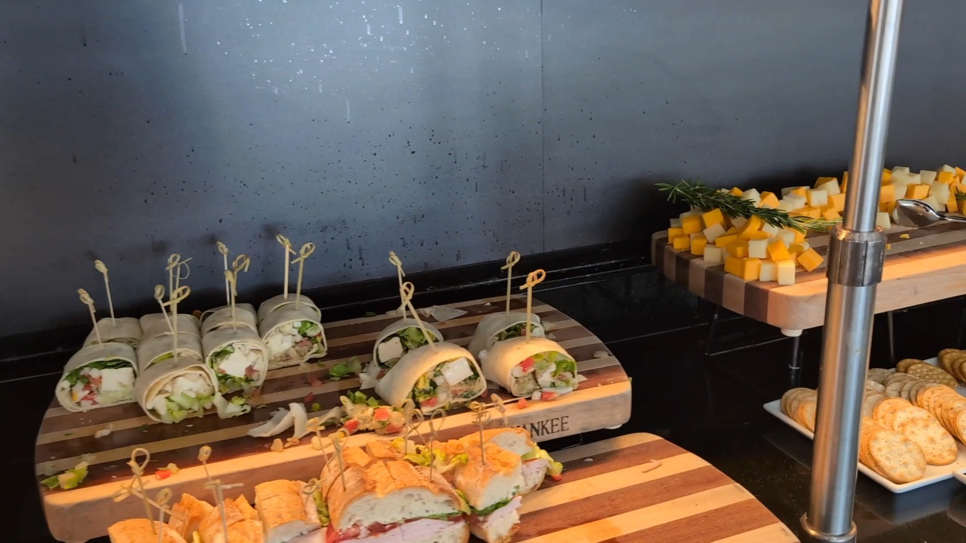 Sandwiches and wraps on butcher-block boards at the United Club at IAH Gate C33, with a small charcuterie of cheese cubes and rosemary on the side.