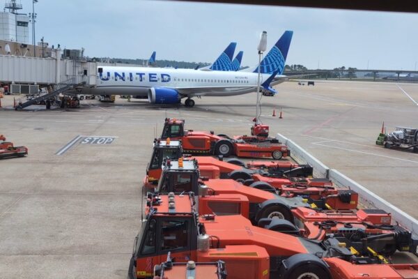 Tarmac view from the United Club at IAH Gate C33 with a United Airlines 737 at the gate and orange ground-equipment tractors lined up below.