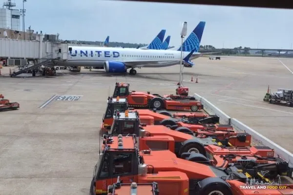 Tarmac view from the United Club at IAH Gate C33 with a United Airlines 737 at the gate and orange ground-equipment tractors lined up below.
