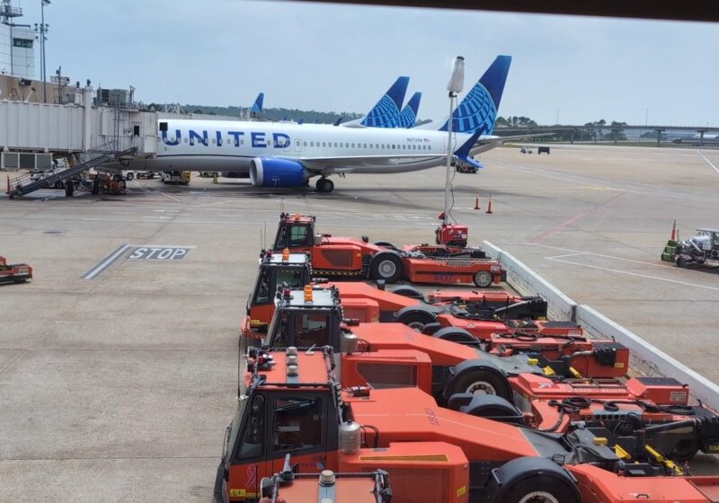Tarmac view from the United Club at IAH Gate C33 with a United Airlines 737 at the gate and orange ground-equipment tractors lined up below.