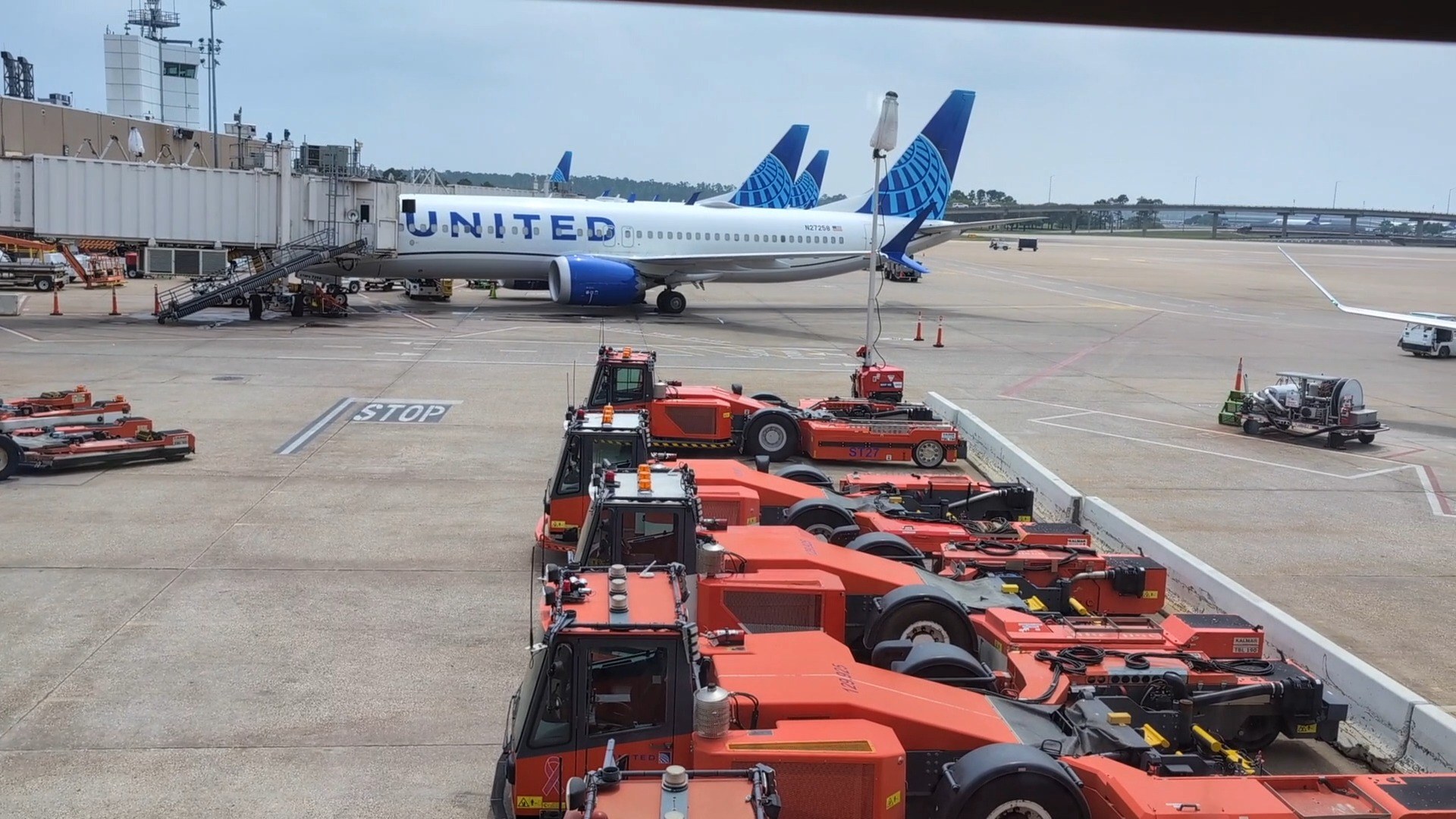 Tarmac view from the United Club at IAH Gate C33 with a United Airlines 737 at the gate and orange ground-equipment tractors lined up below.