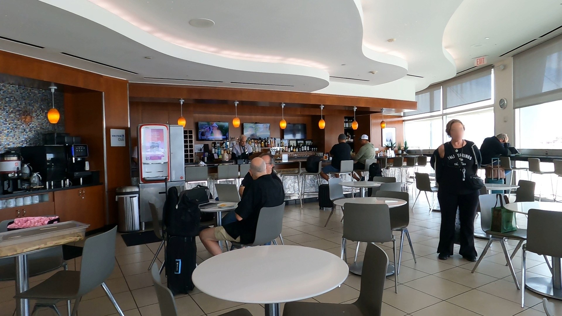 Full bar at the United Club LAS with overhead TVs and a coffee station to the left