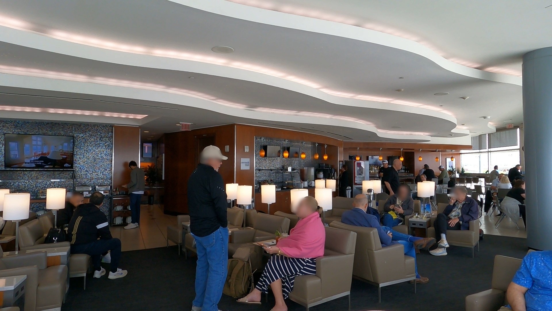 Wide view of the United Club LAS lounge with a blue mosaic feature wall and a TV mounted above seating