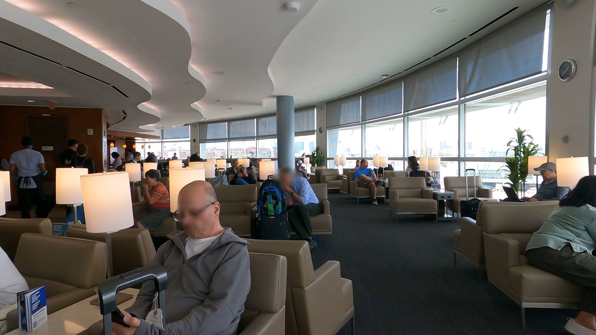 Wide view of the United Club seating area at LAS with curved ceiling lights, table lamps and large windows