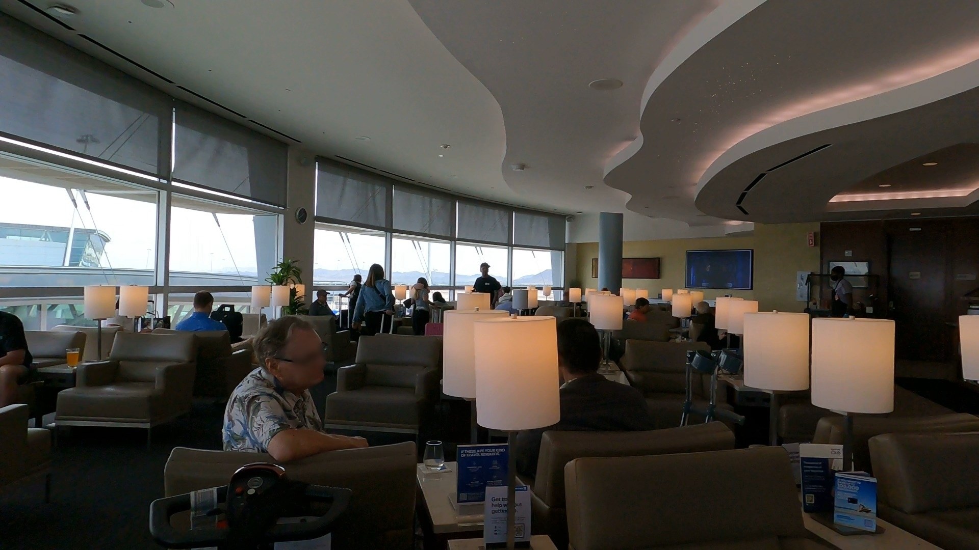 Lounge seating at the United Club LAS with table lamps along the window line and desert mountains visible through the glass