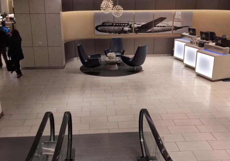 Vintage United Mainliner Convair photo mural behind three black swivel chairs at the United Club at ORD Gate B18, with the illuminated check-in podiums on the right.