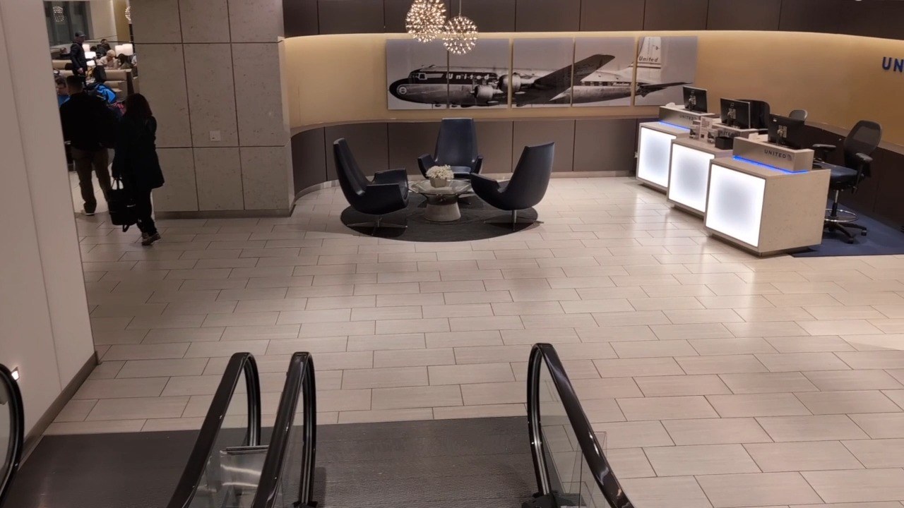 Vintage United Mainliner Convair photo mural behind three black swivel chairs at the United Club at ORD Gate B18, with the illuminated check-in podiums on the right.