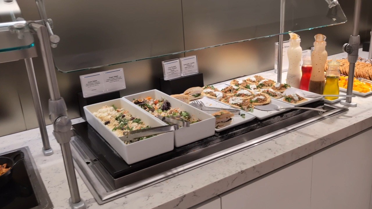 Salad bar at the United Club at ORD Gate B18 with grain salads, mixed greens, mediterranean flatbreads, and a row of dressing bottles on the right.