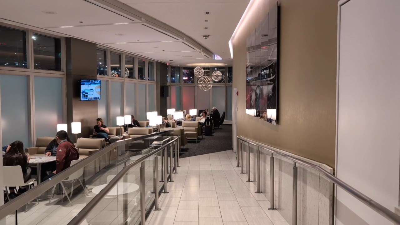 Seating area at the United Club at ORD Gate B18 with starburst chandeliers, beige leather chairs, and lamps on side tables.