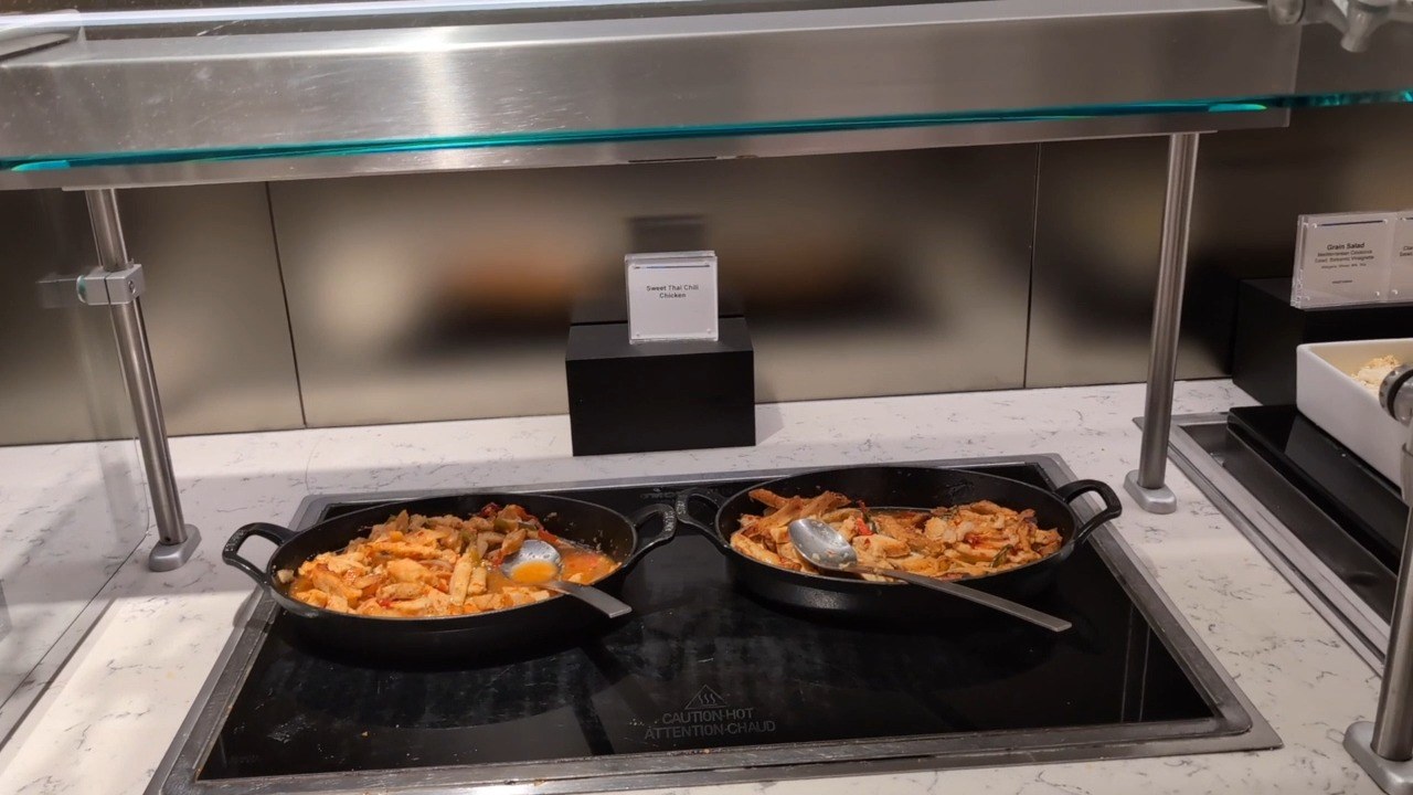 Sweet Thai Chili Chicken in a cast-iron skillet on the hot food counter at the United Club at ORD Gate B18, with a second skillet of stir-fry alongside.