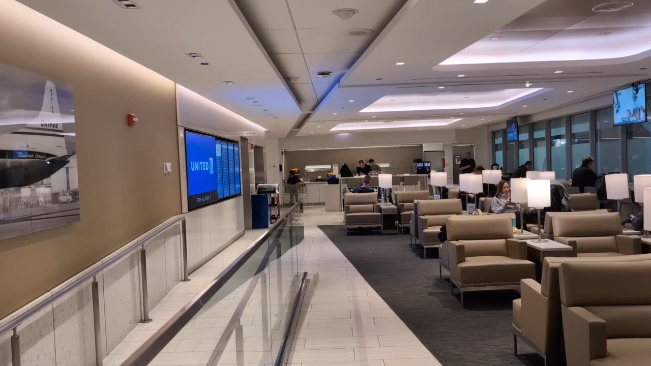 Main seating area at the United Club at ORD Gate B18 with tan leather club chairs, lamps on side tables, and historical United airplane photography on the left wall.