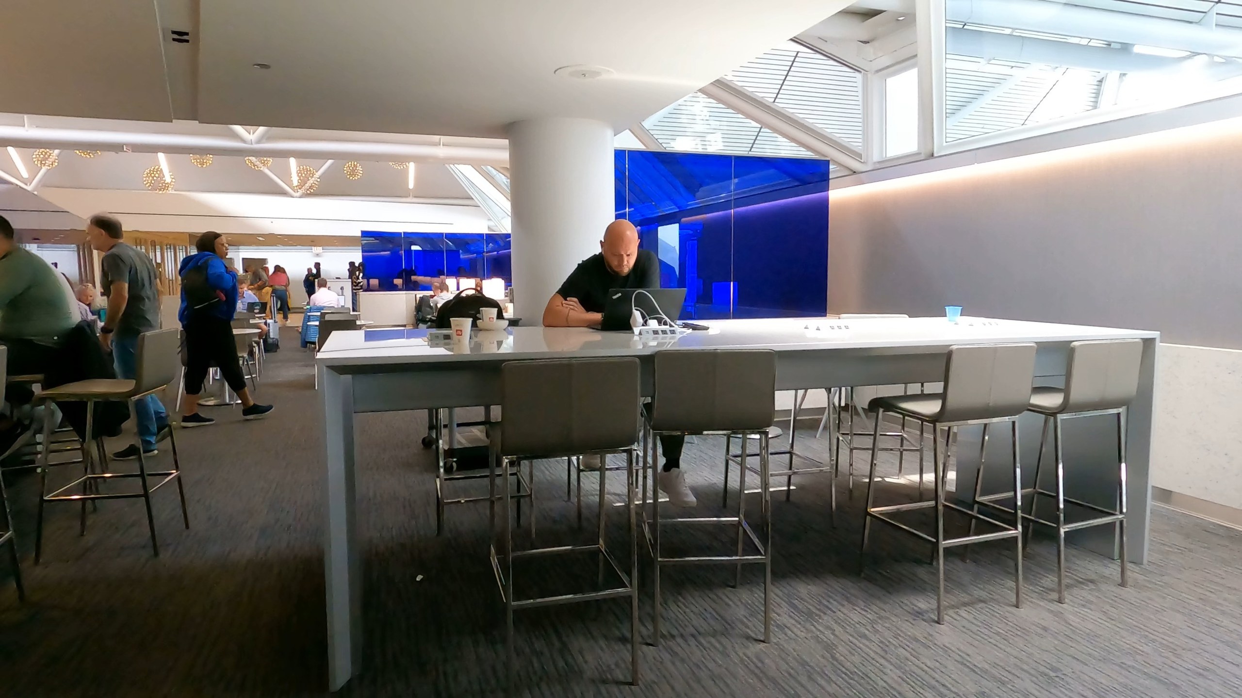 A long marble communal high-top at the United Club at ORD Gate B6 with metal stools and the blue glass divider wall in the background.