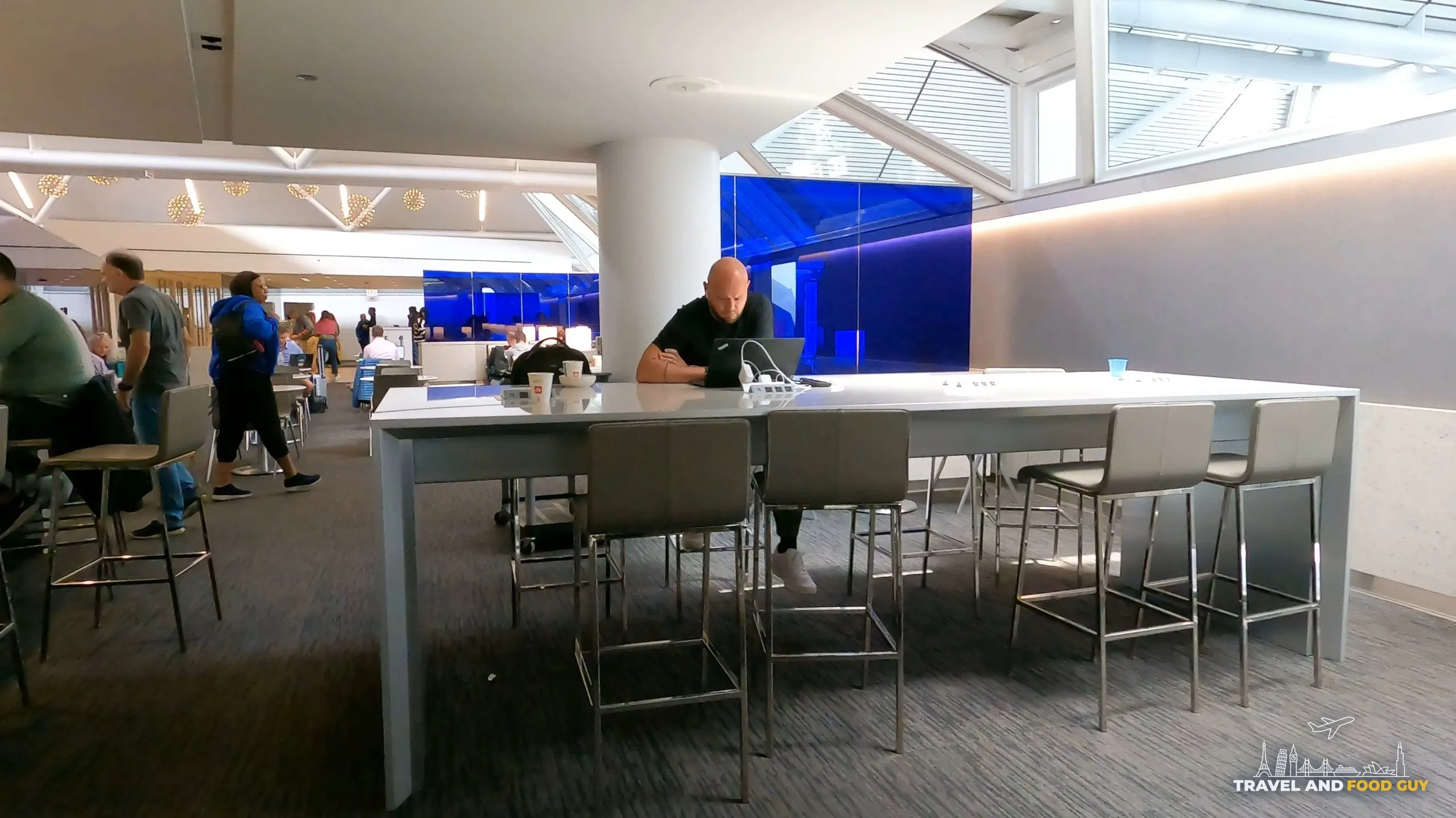 A long marble communal high-top at the United Club at ORD Gate B6 with metal stools and the blue glass divider wall in the background.