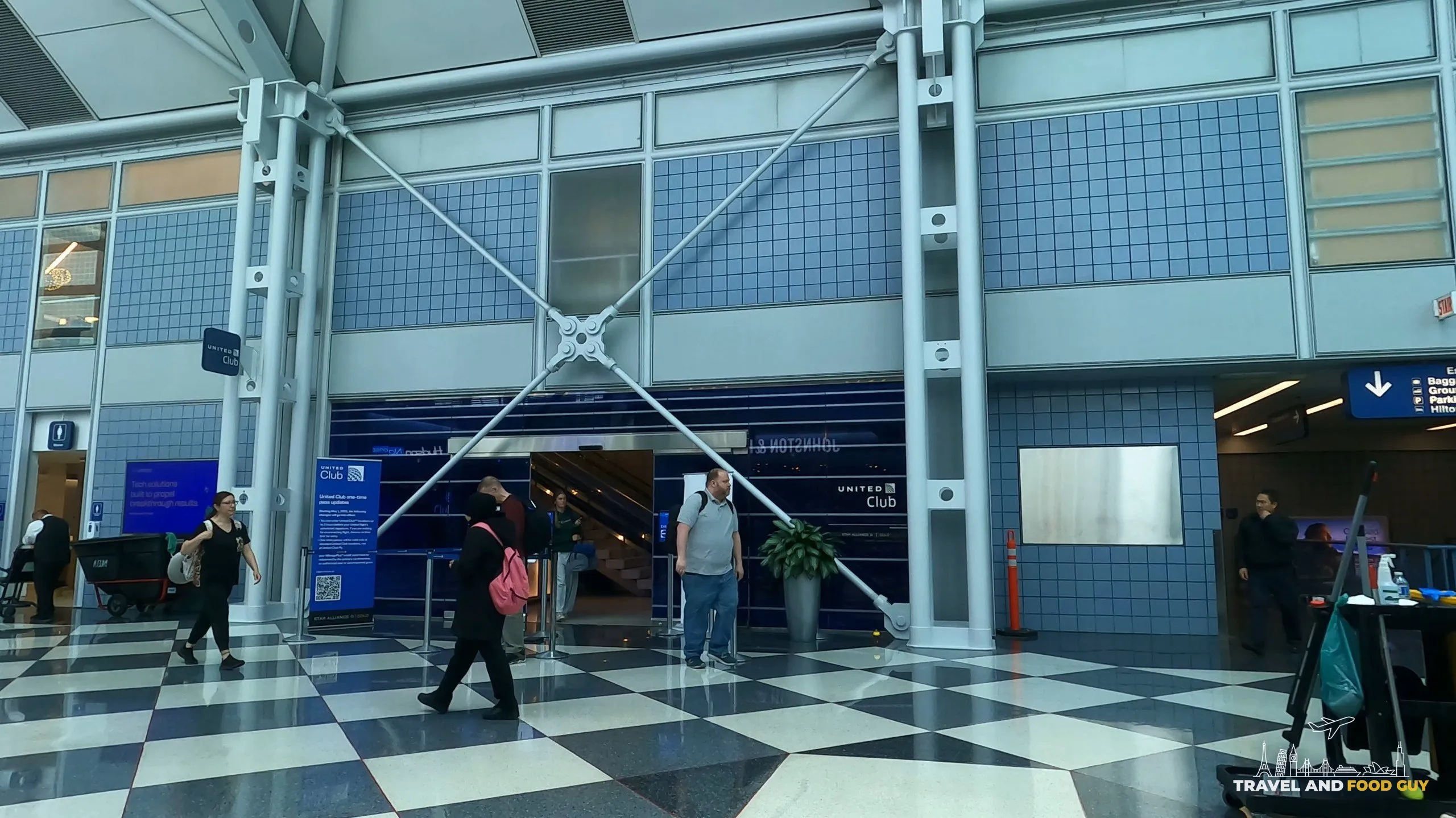 Exterior view of the United Club at ORD Gate B6 from the concourse below, with the black-and-white checkerboard floor in the foreground and the United Club entrance flanked by structural braces.