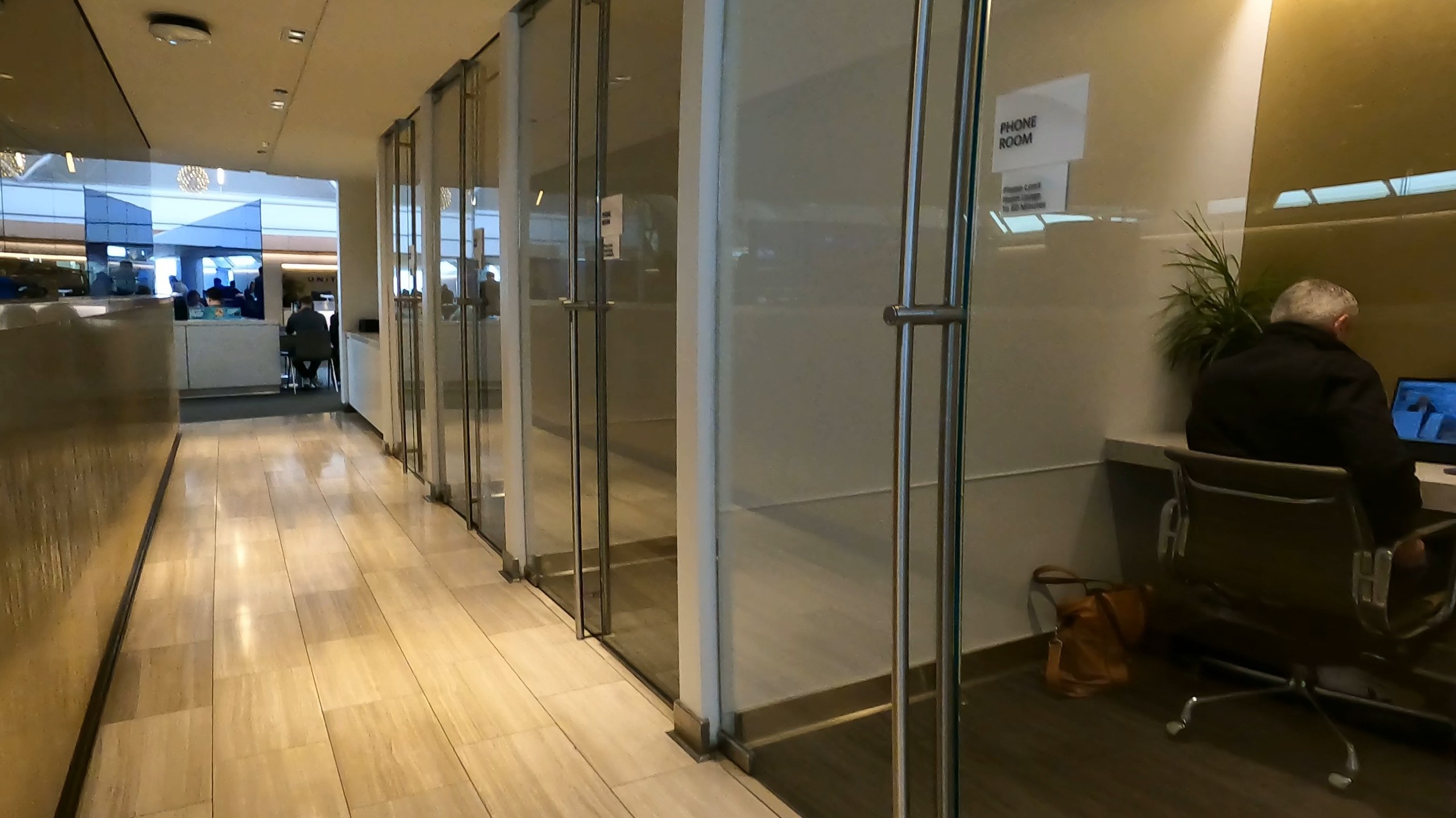 Hallway of glass-walled phone rooms at the United Club at ORD Gate B6, each clearly labeled PHONE ROOM and outfitted with a desk and task chair.
