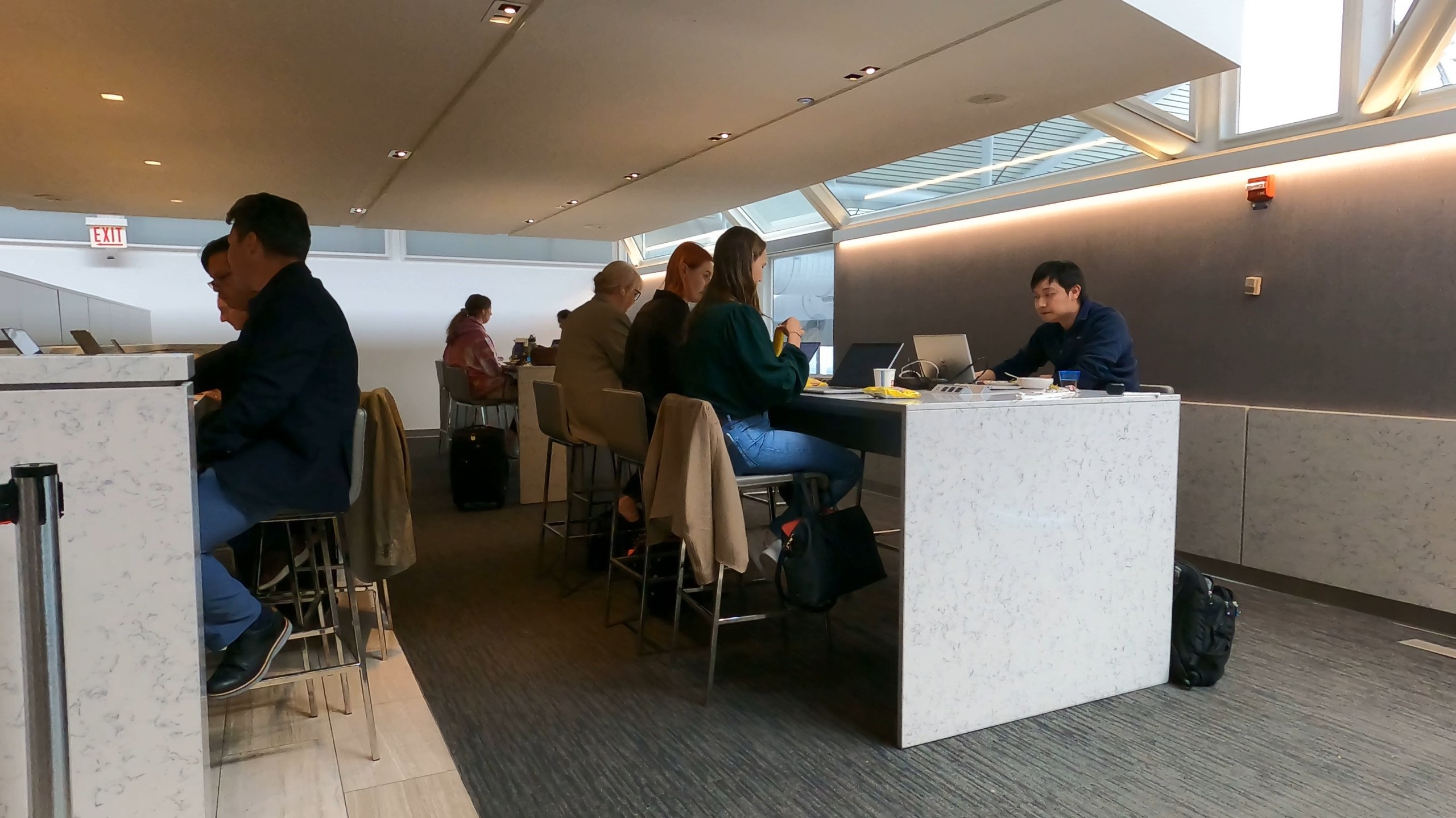 Marble communal high-tops at the United Club at ORD Gate B6, with travelers working on laptops under the skylit ceiling.