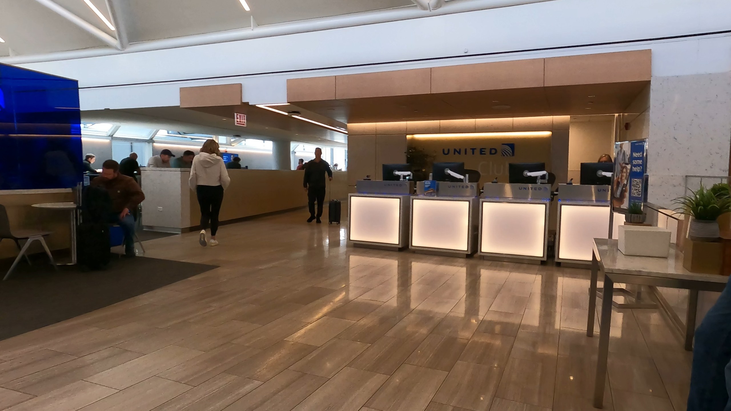 Reception at the United Club at ORD Gate B6 with the United logo on the back wall and four illuminated frosted-glass check-in podiums in front.