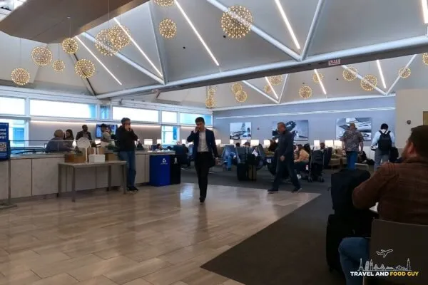 Main seating area at the United Club at ORD Gate B6 with the signature starburst chandeliers overhead, the food counter on the left, and historical United airplane photography on the wall.
