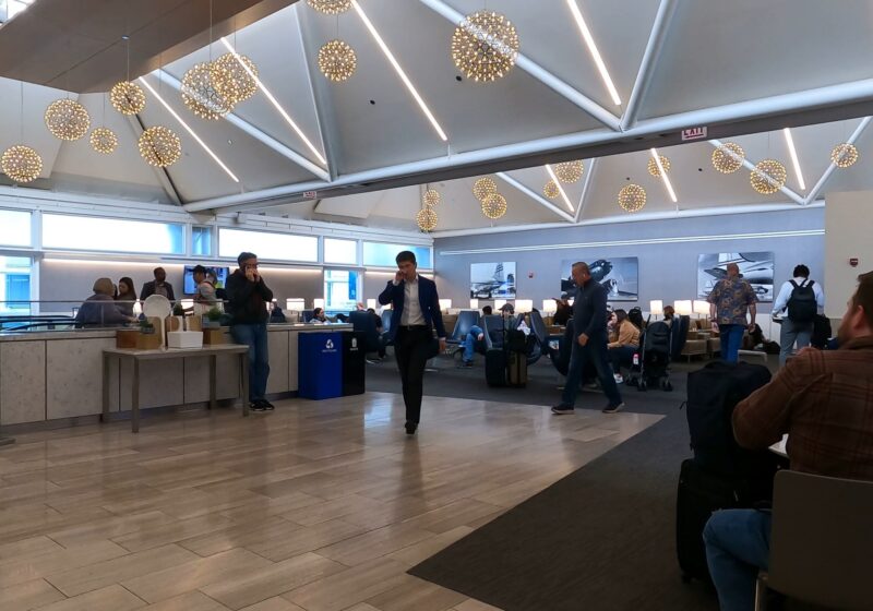 Main seating area at the United Club at ORD Gate B6 with the signature starburst chandeliers overhead, the food counter on the left, and historical United airplane photography on the wall.