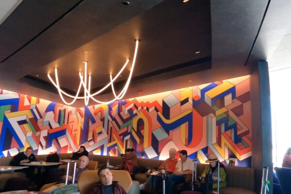 The signature commissioned abstract art mural at the United Club at ORD Concourse C, with the curved neon ceiling sculpture above the seating banquette in the foreground.