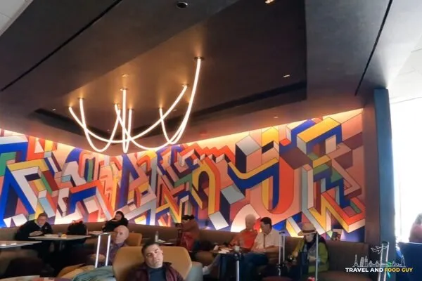 The signature commissioned abstract art mural at the United Club at ORD Concourse C, with the curved neon ceiling sculpture above the seating banquette in the foreground.