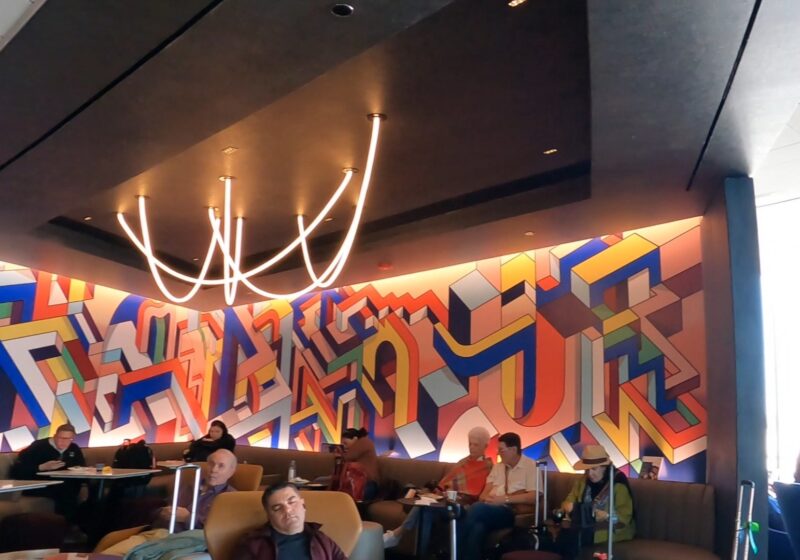 The signature commissioned abstract art mural at the United Club at ORD Concourse C, with the curved neon ceiling sculpture above the seating banquette in the foreground.