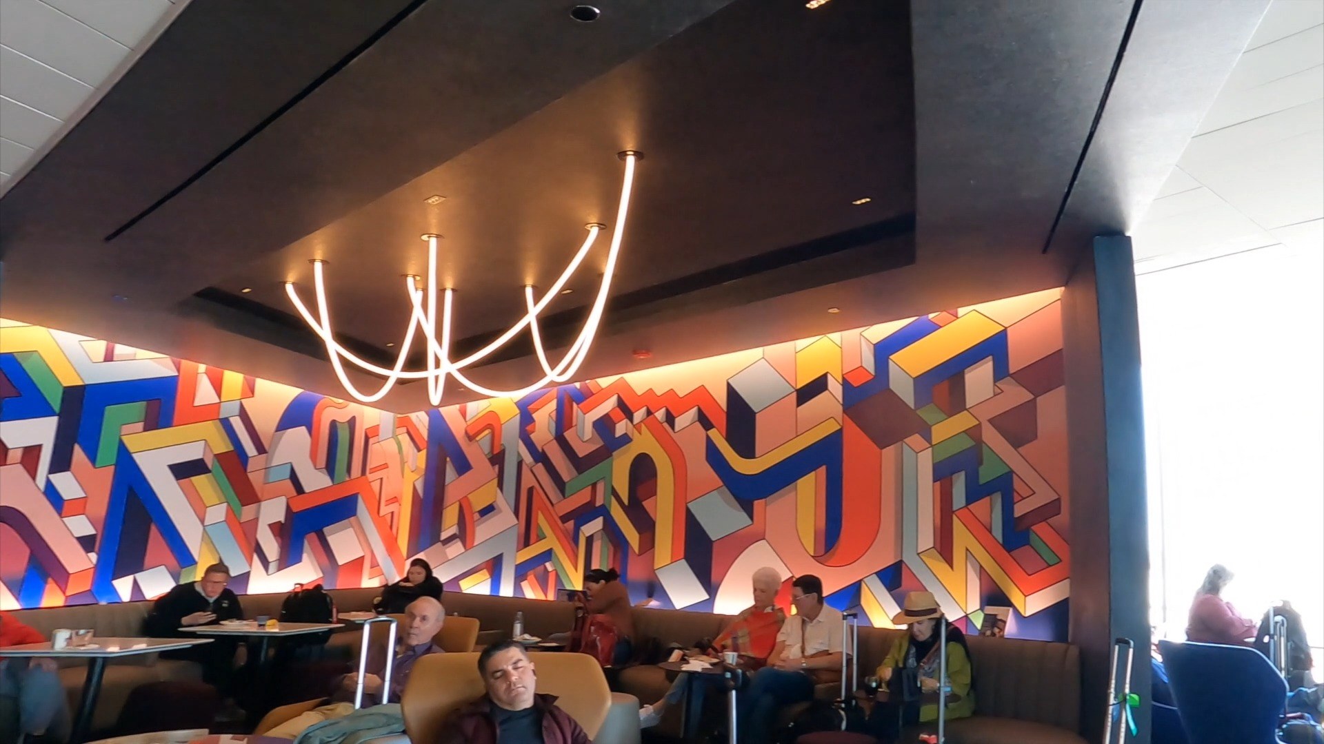 The signature commissioned abstract art mural at the United Club at ORD Concourse C, with the curved neon ceiling sculpture above the seating banquette in the foreground.