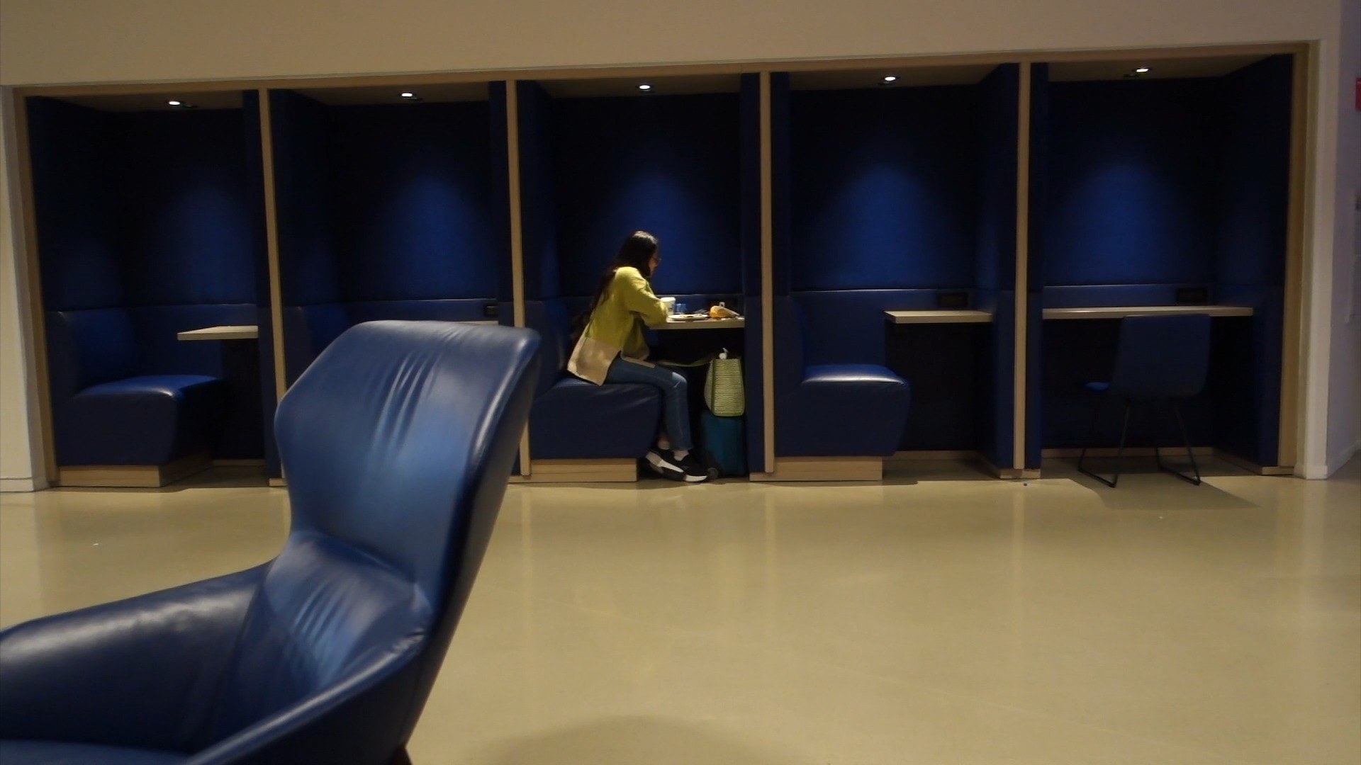 Row of high-backed blue leather work pods with desks at the United Club at ORD Concourse C, a quiet zone for laptop work pre-flight.
