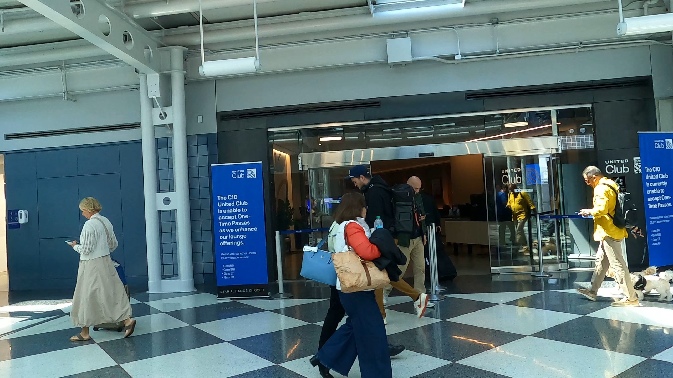 Exterior entrance to the United Club at ORD Concourse C, with the C10 United Club one-time-pass updates banner and travelers walking past on the checkerboard floor.