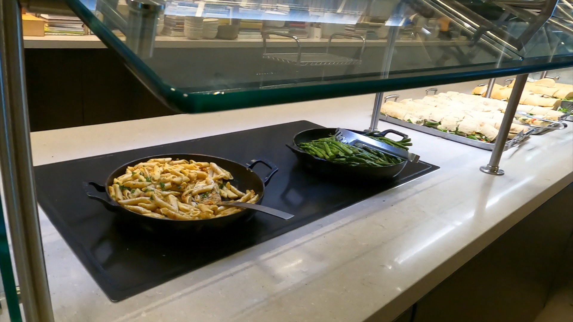 Hot food at the United Club at ORD Concourse C, with a cast-iron skillet of penne pasta with chicken and a smaller skillet of seasoned green beans beside it.