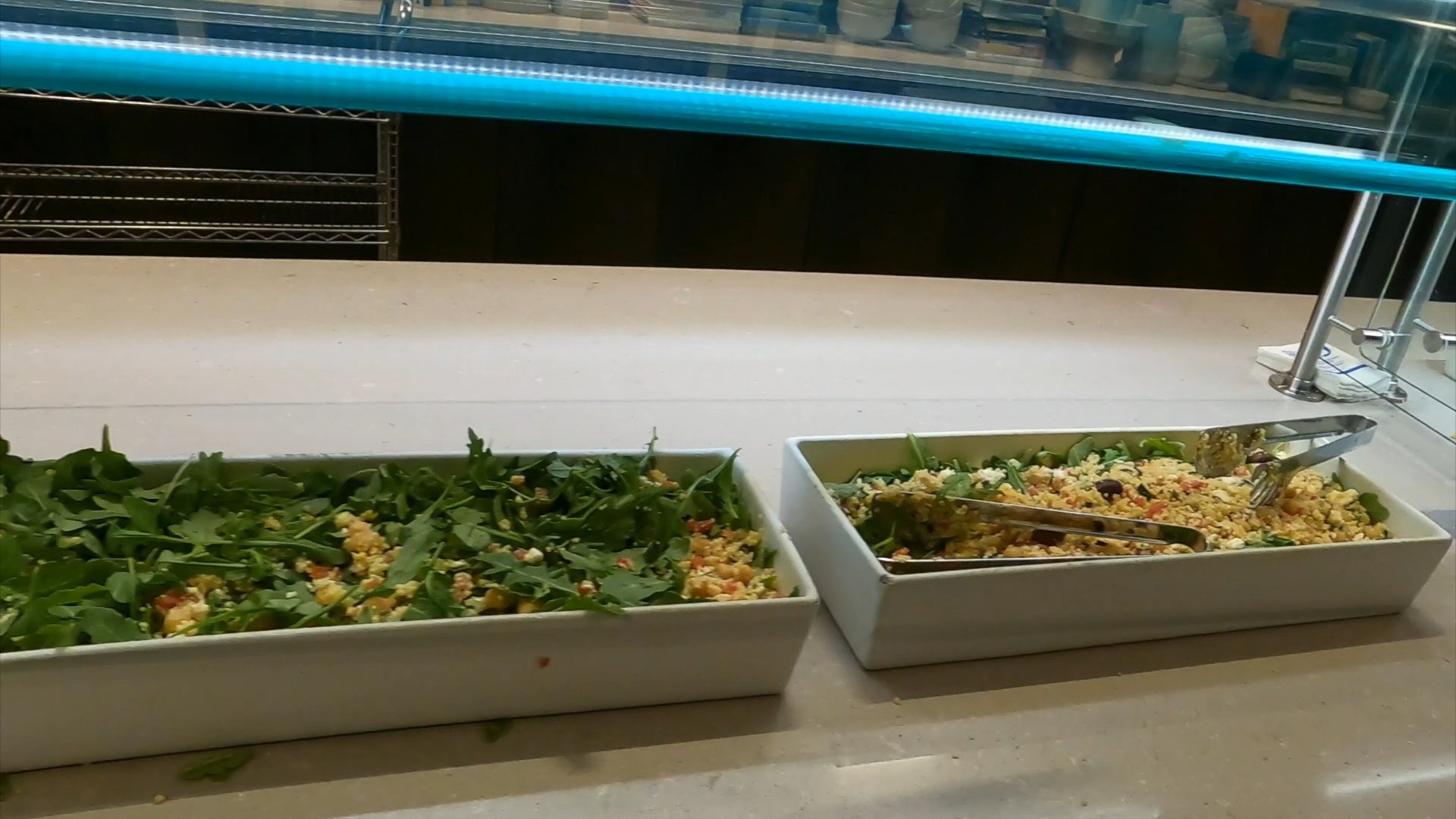 Salad bar at the United Club at ORD Concourse C with one tray of arugula and one tray of grain salad with greens.