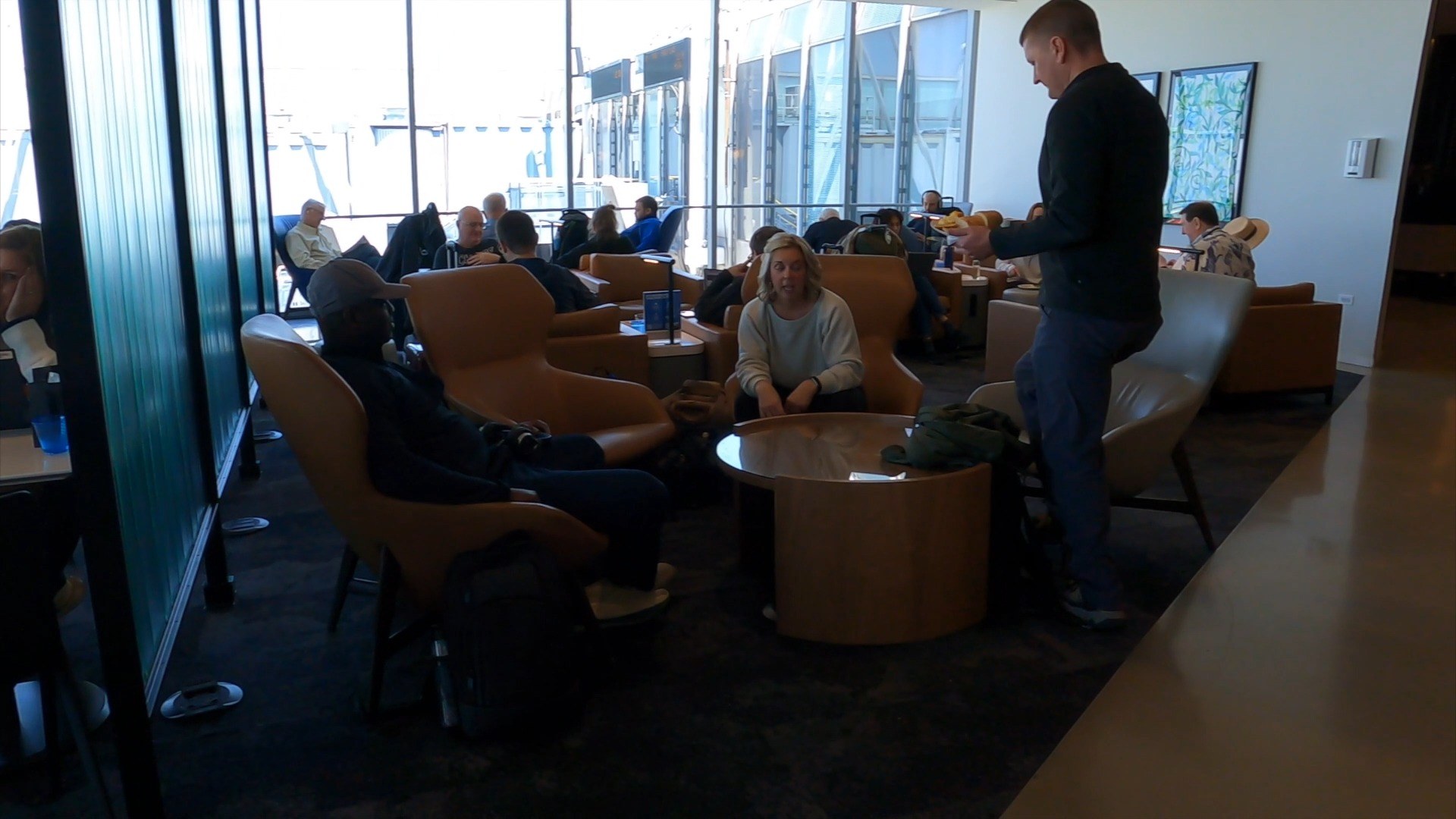 Cluster of tan leather club chairs at the United Club at ORD Concourse C with travelers in conversation and a server passing through.